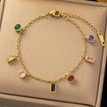 A gold chain bracelet with multiple colorful gemstone charms, displayed on a beige jewelry box. The charms include round and rectangular bezel-set stones in green, purple, yellow, pink, red, and dark blue.