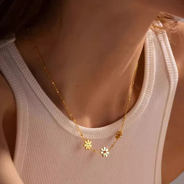 Gold necklace with floral pendants worn by a person in a white tank top.