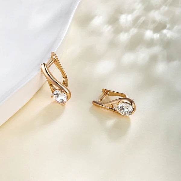 Gold earrings with clear gemstones on a soft white background