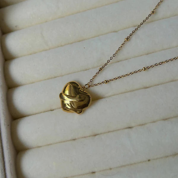 Gold necklace with a heart-shaped pendant on a white textured surface