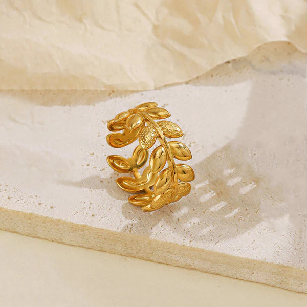 Gold leaf-shaped earring on a textured beige surface