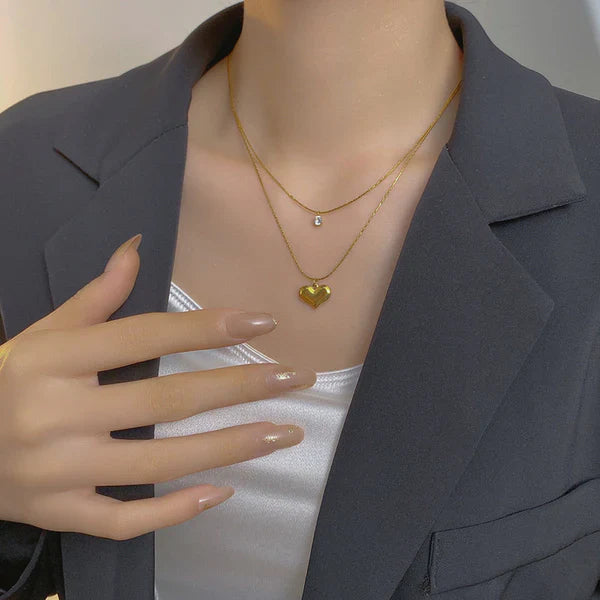 Person wearing a gold necklace with a heart pendant, with a hand adjusting the blazer.