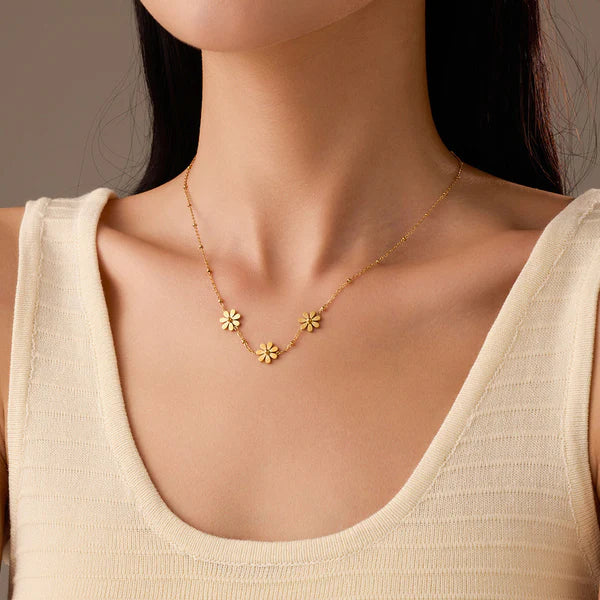 Gold necklace with floral pendants on a person wearing a beige top.