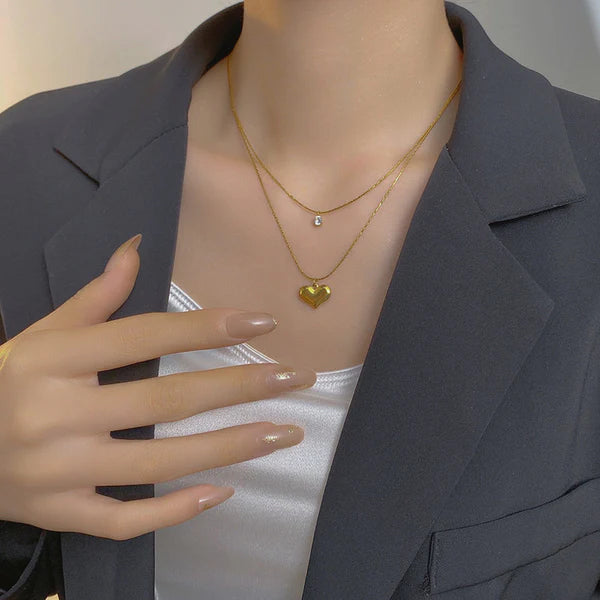 Person wearing a gold necklace with a heart pendant, with a hand adjusting the blazer.