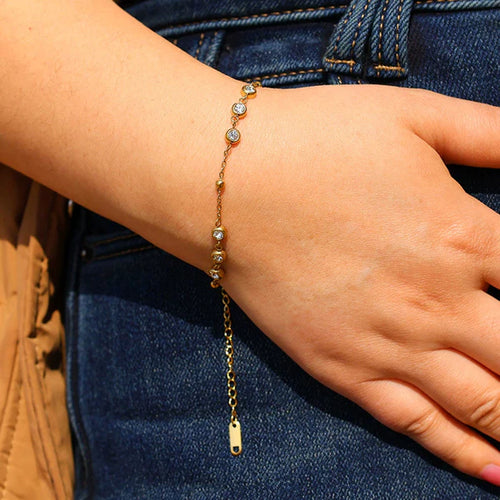 Gold bracelet with small stones on a wrist against a denim background