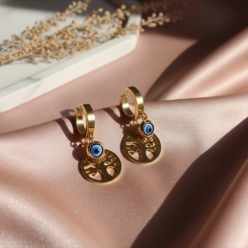 Gold hoop earrings with blue eye design on a pink satin surface