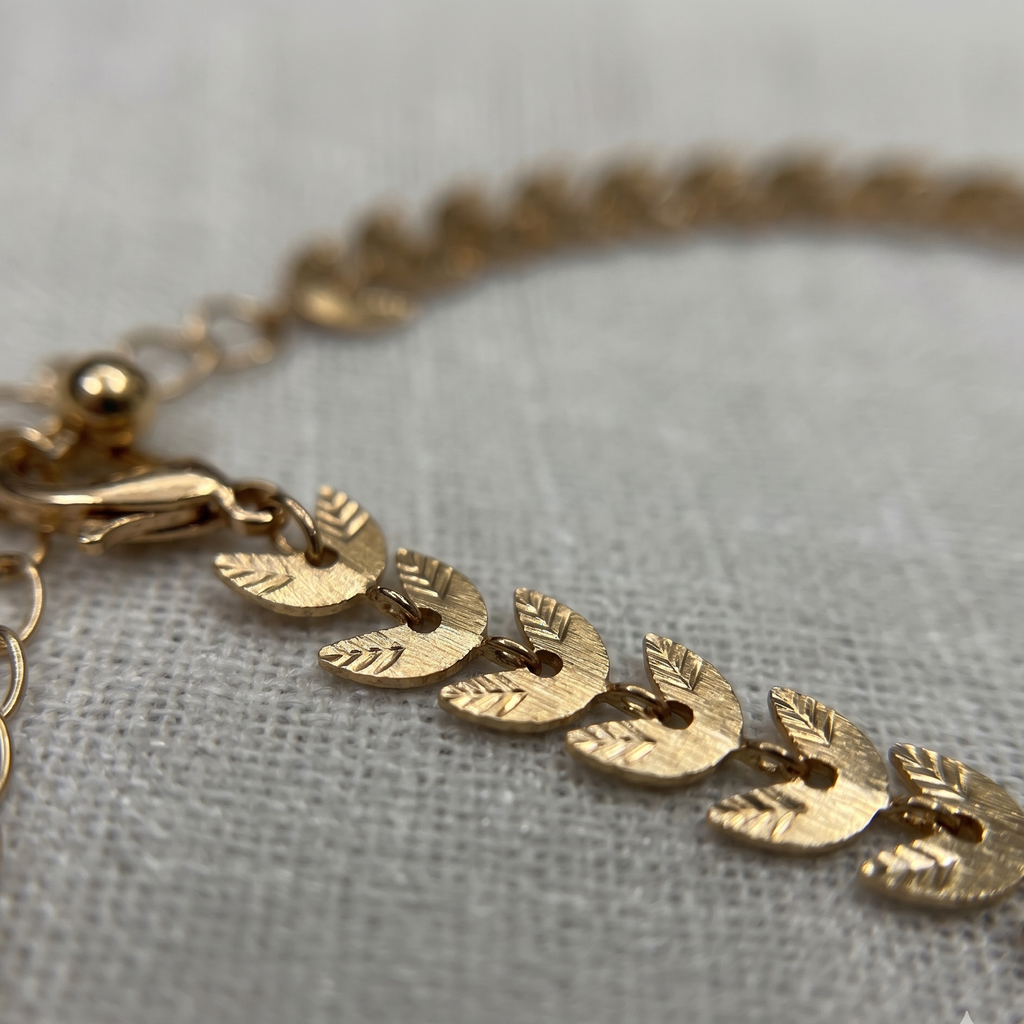 Gold bracelet with leaf-shaped charms on a light gray fabric background