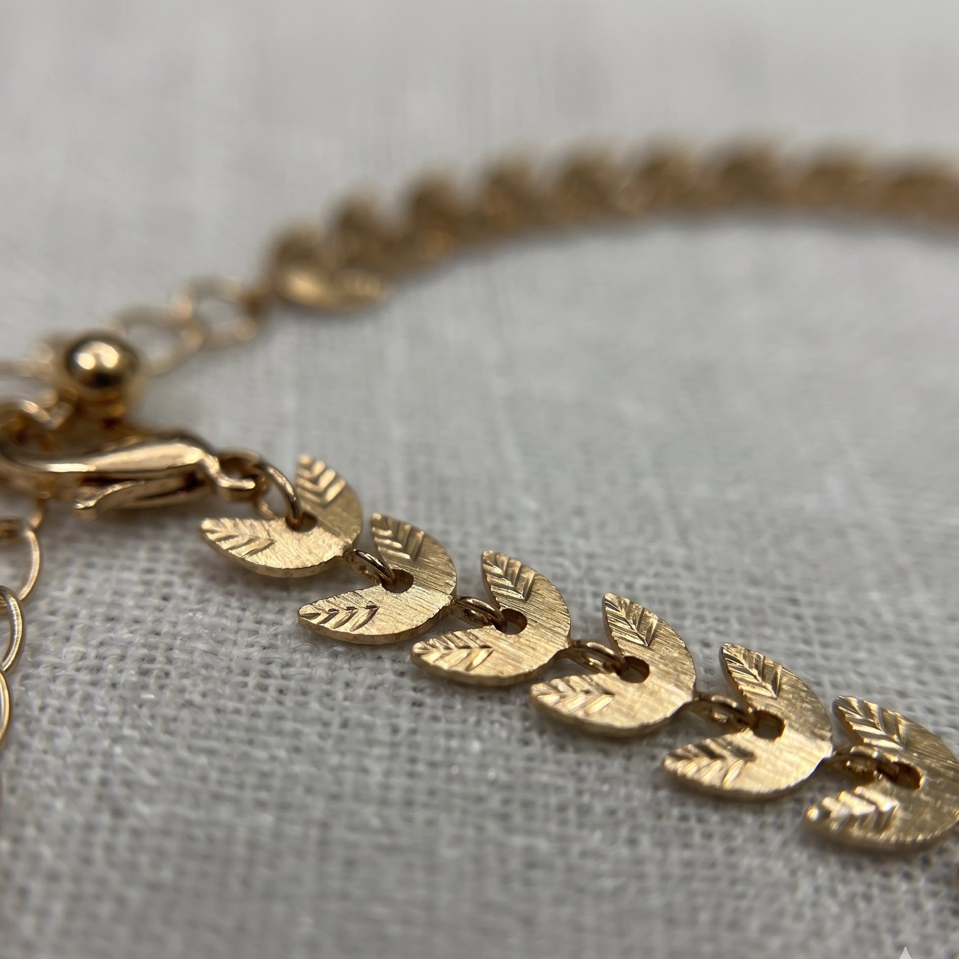 Gold bracelet with leaf-shaped charms on a light gray fabric background