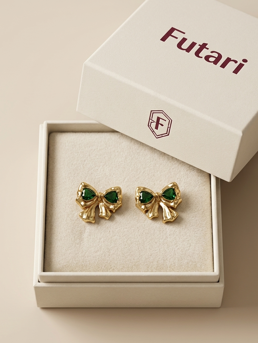 Gold bow-shaped earrings with green gemstones in a 'Futari' branded box.