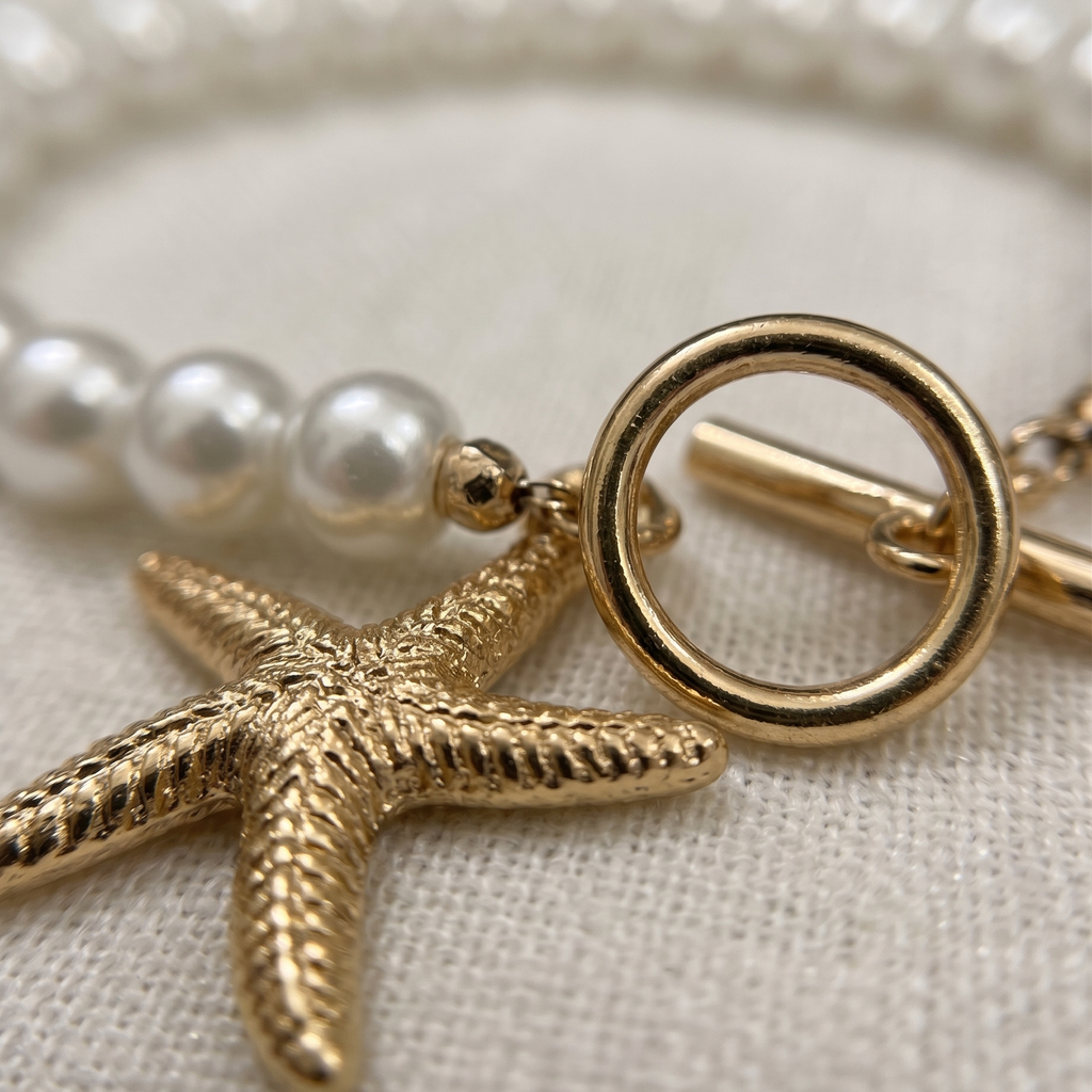 Pearl bracelet with a gold starfish charm on a neutral background
