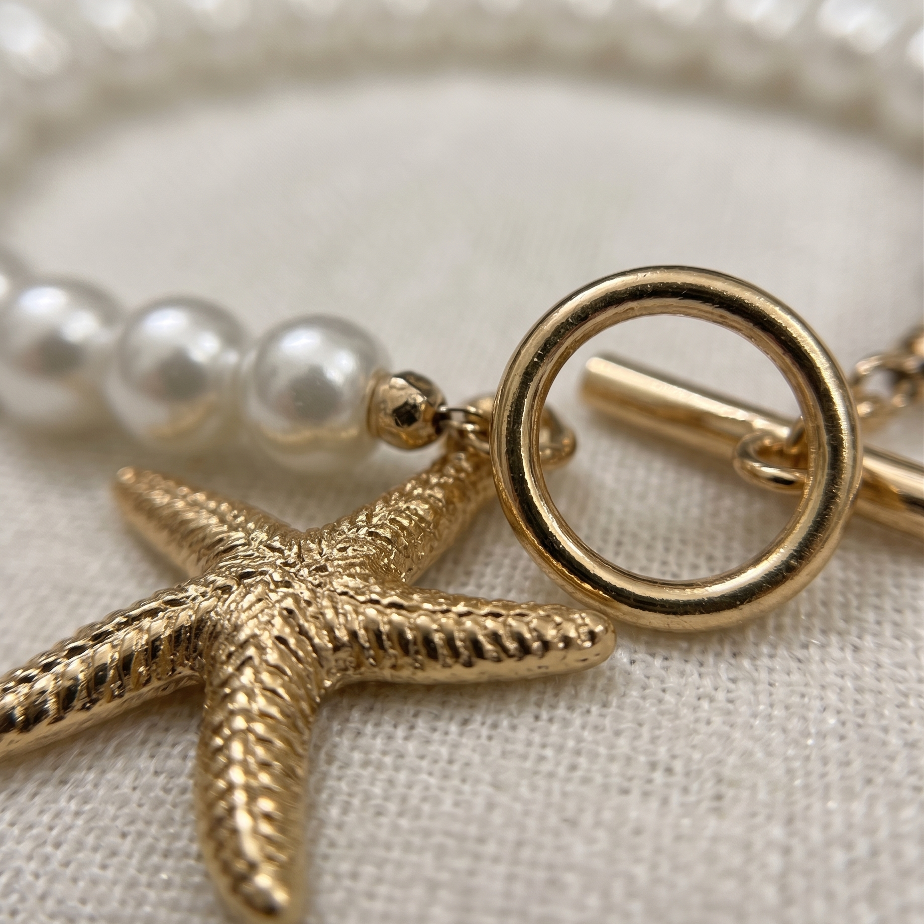 Pearl bracelet with a gold starfish charm on a neutral background