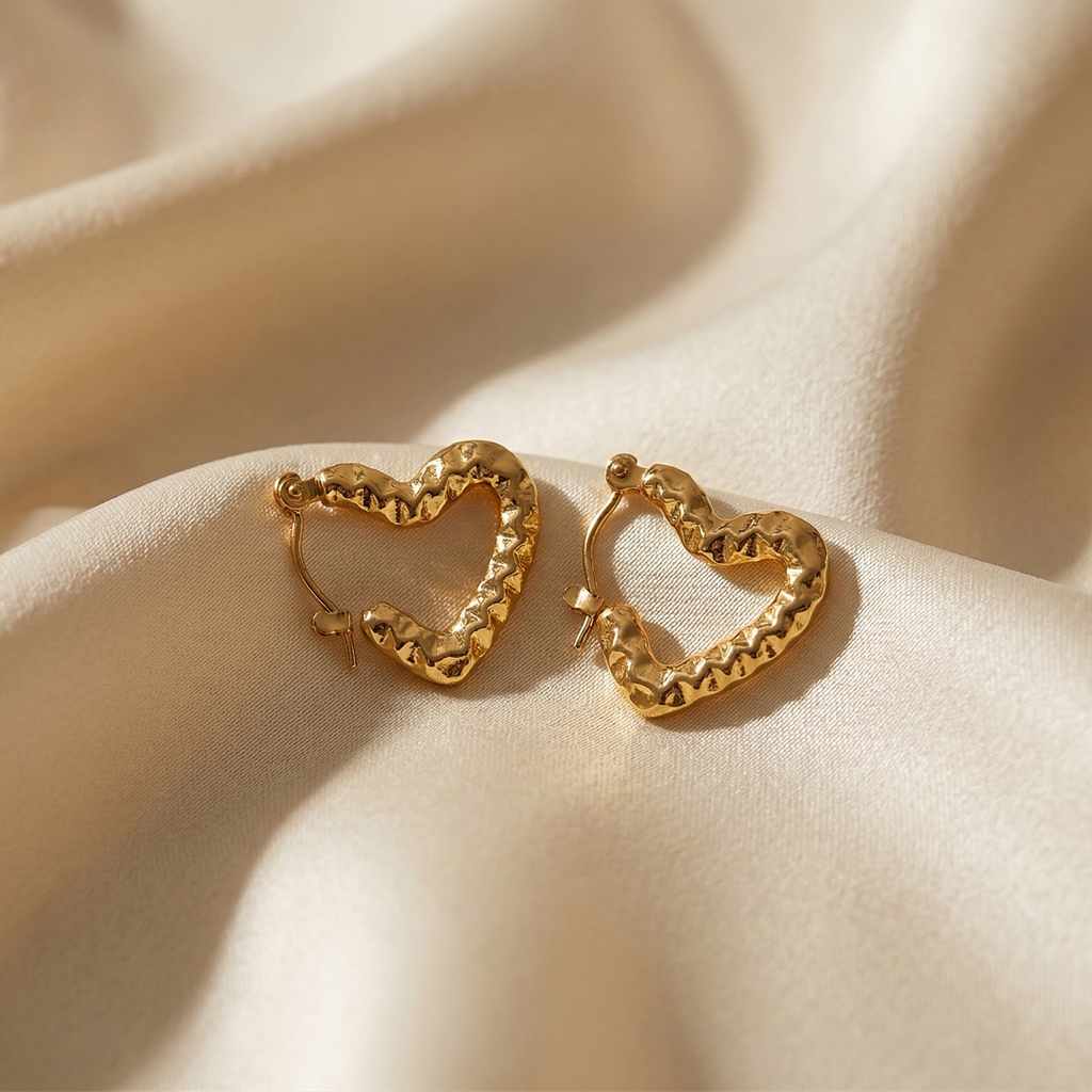 Gold heart-shaped earrings on a beige fabric background