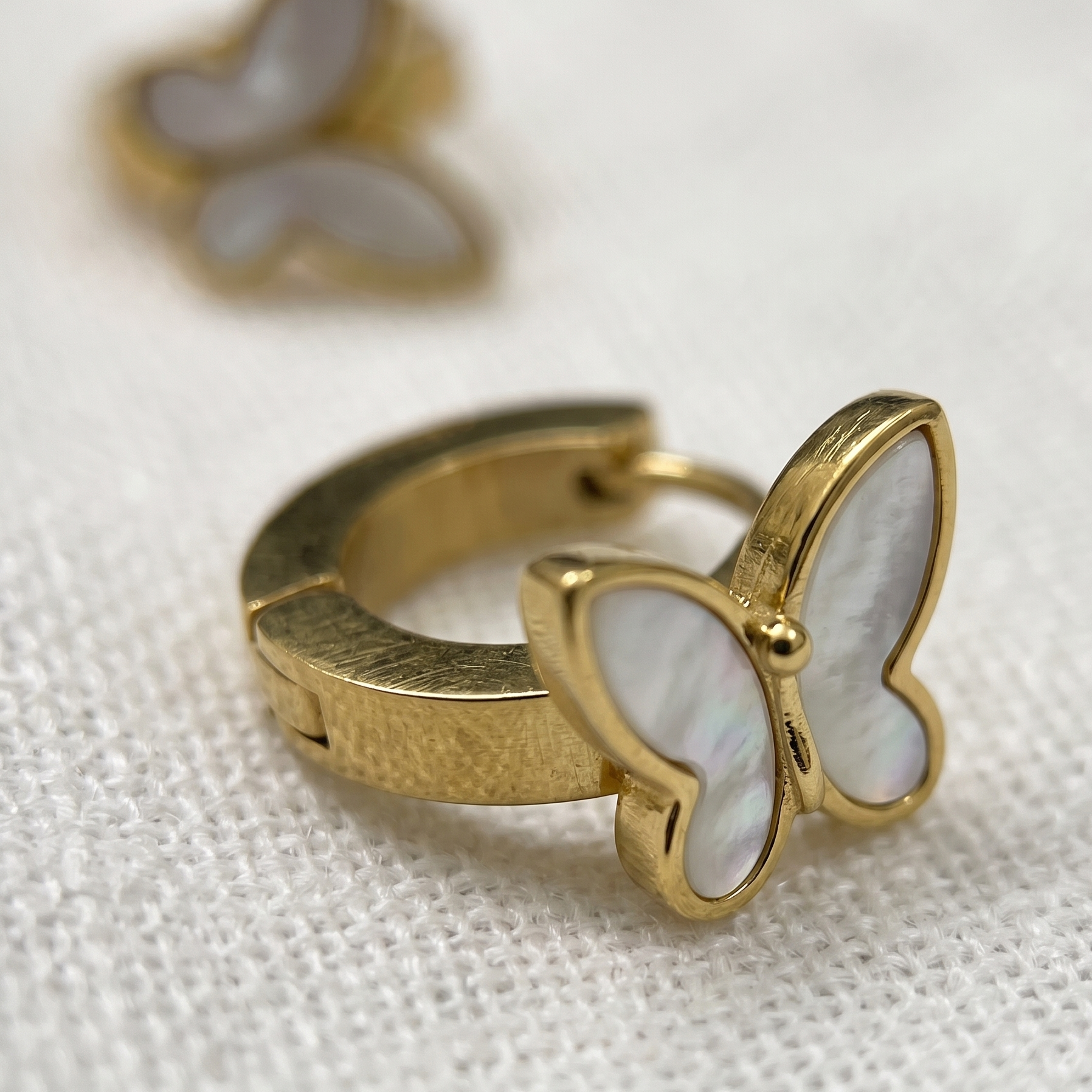 Gold butterfly-shaped earrings on a textured white background