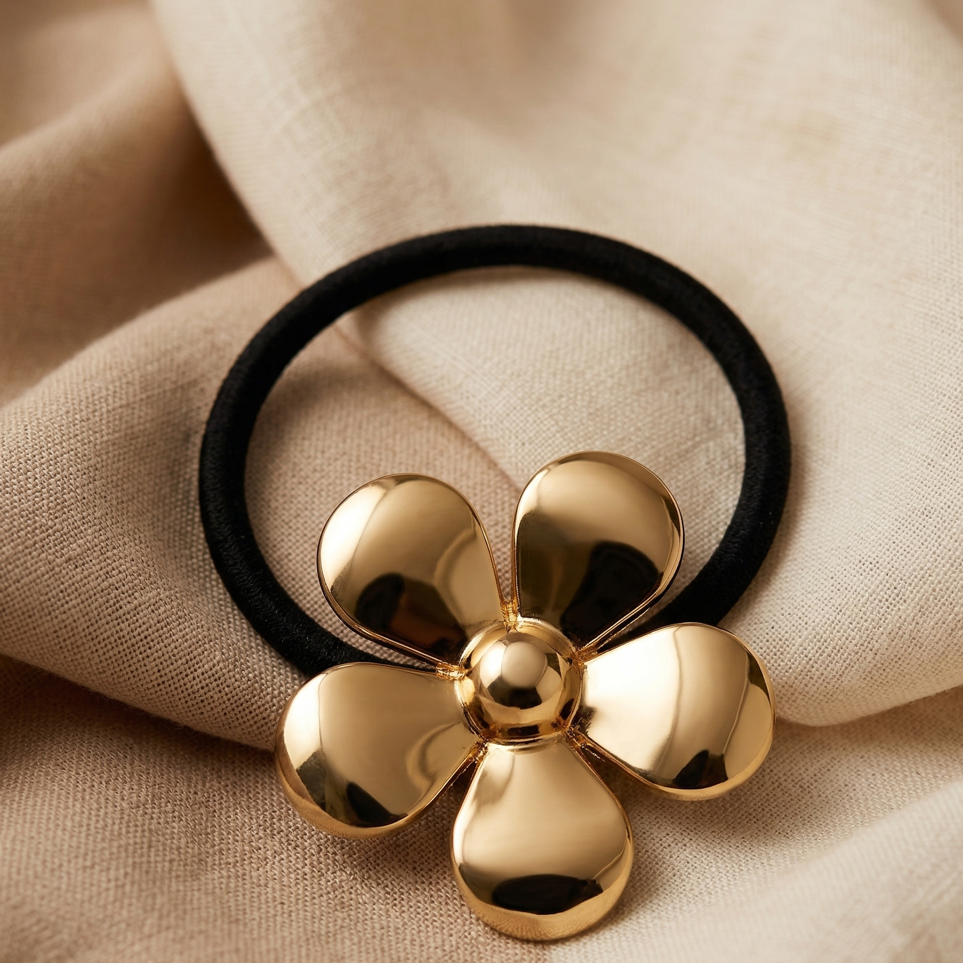 Gold flower-shaped hair tie on a beige fabric background