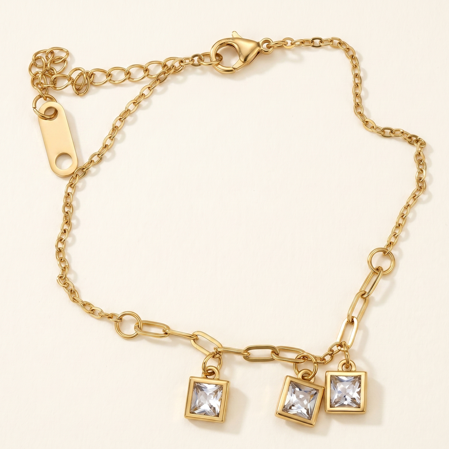 Gold bracelet with square charm on a beige background
