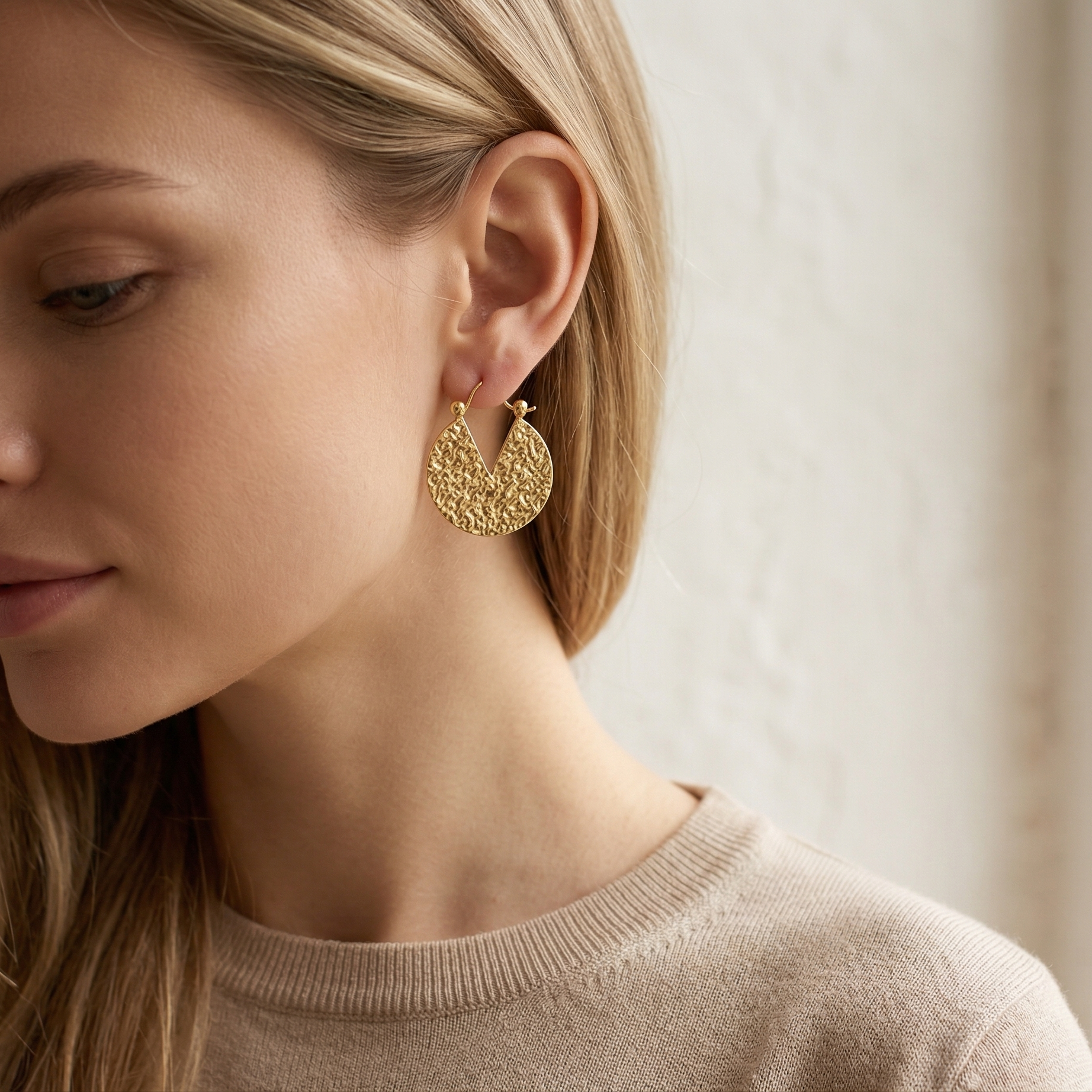 Woman wearing gold earrings with a neutral background