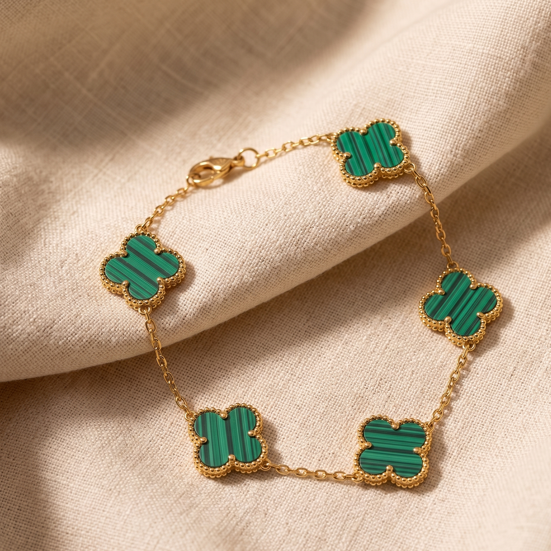 Gold bracelet with green clover-shaped charms on a beige fabric background