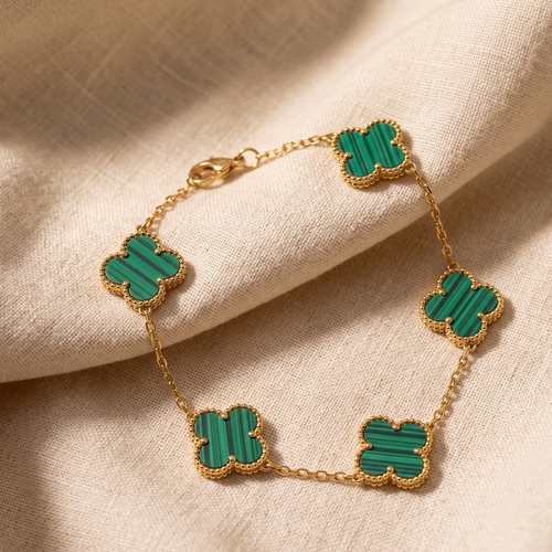 Gold bracelet with green clover-shaped charms on a beige fabric background