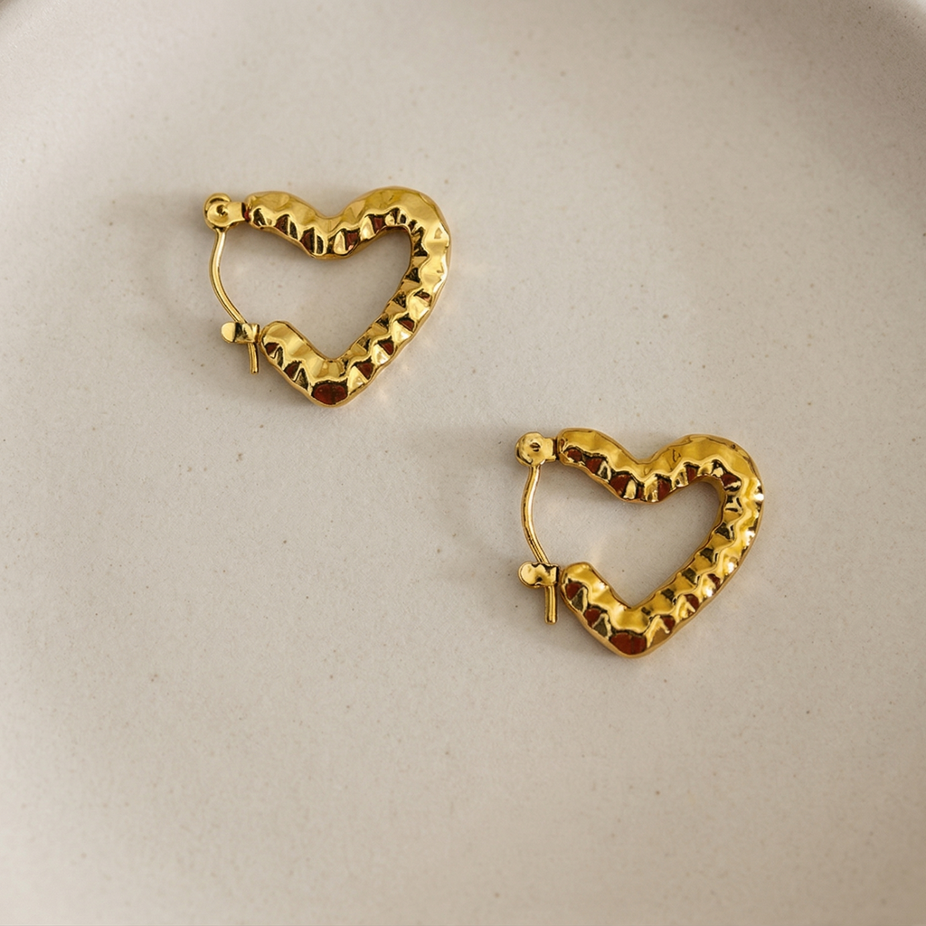 Gold heart-shaped hoop earrings on a beige plate