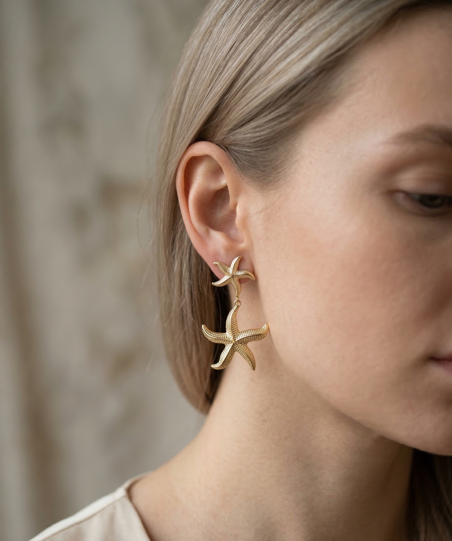 Gold starfish earrings worn by a person with a neutral background