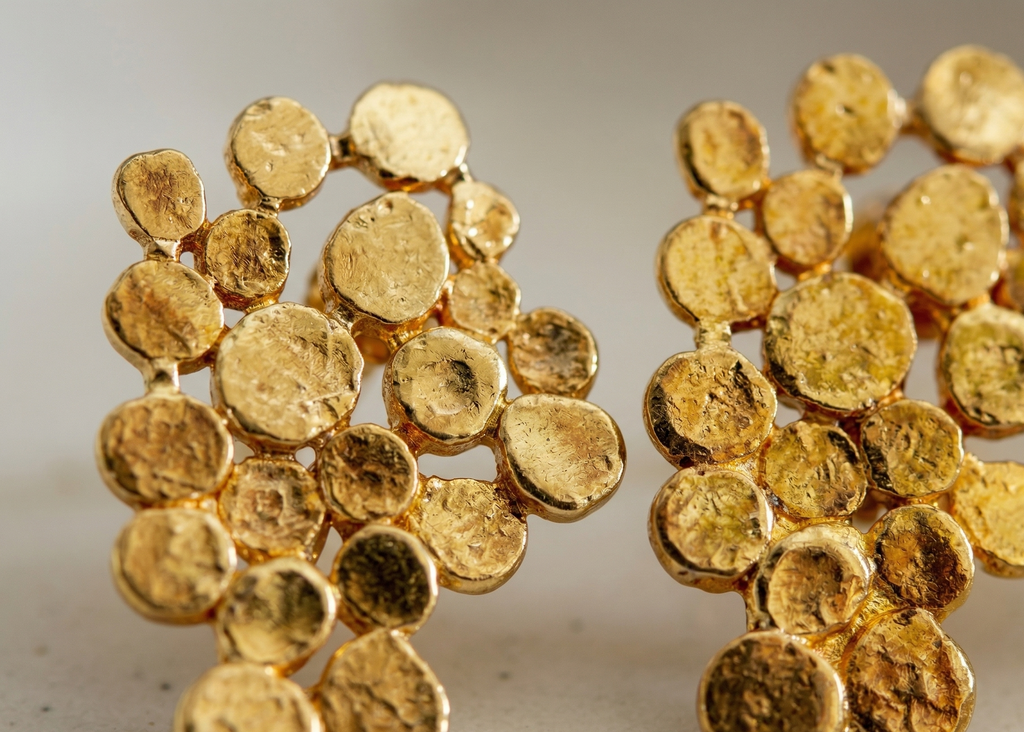 Close-up of gold earrings with a textured design on a neutral background
