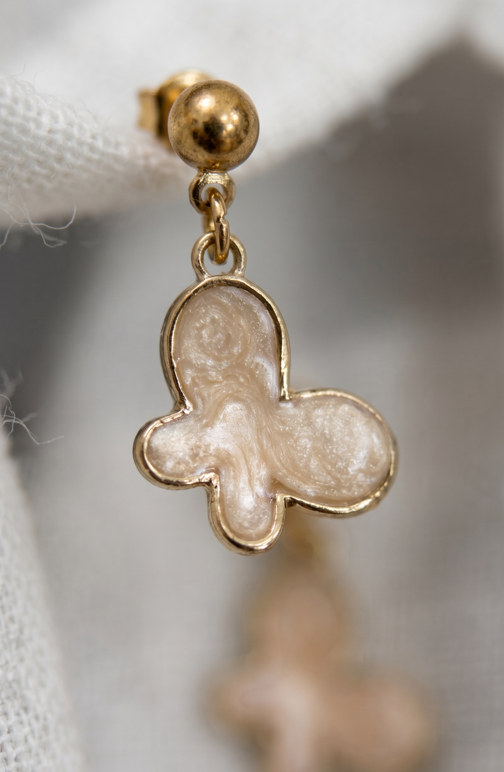 Gold butterfly-shaped earring with a pearl-like center on a blurred background