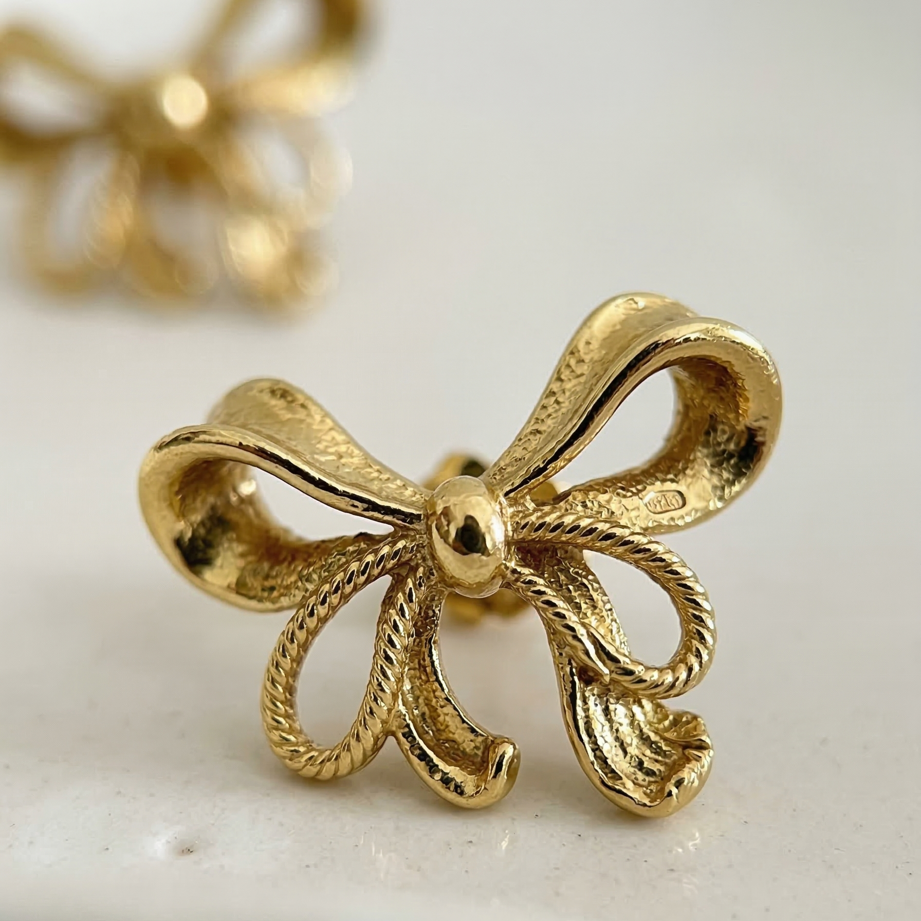 Gold bow-shaped earring on a light background