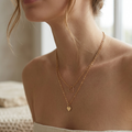 Woman wearing a gold necklace with heart pendants against a neutral background
