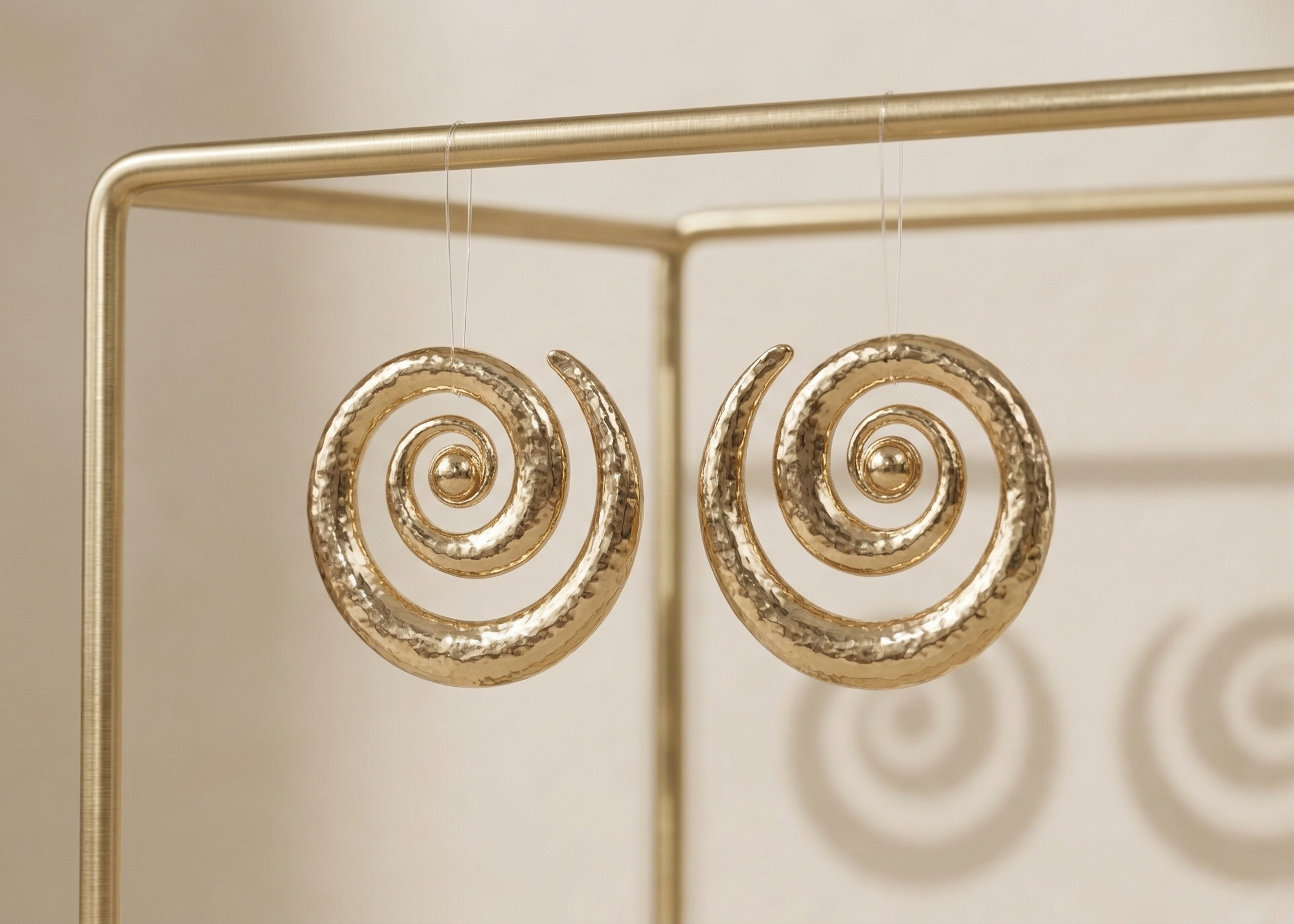 Gold spiral earrings on a gold stand against a beige background