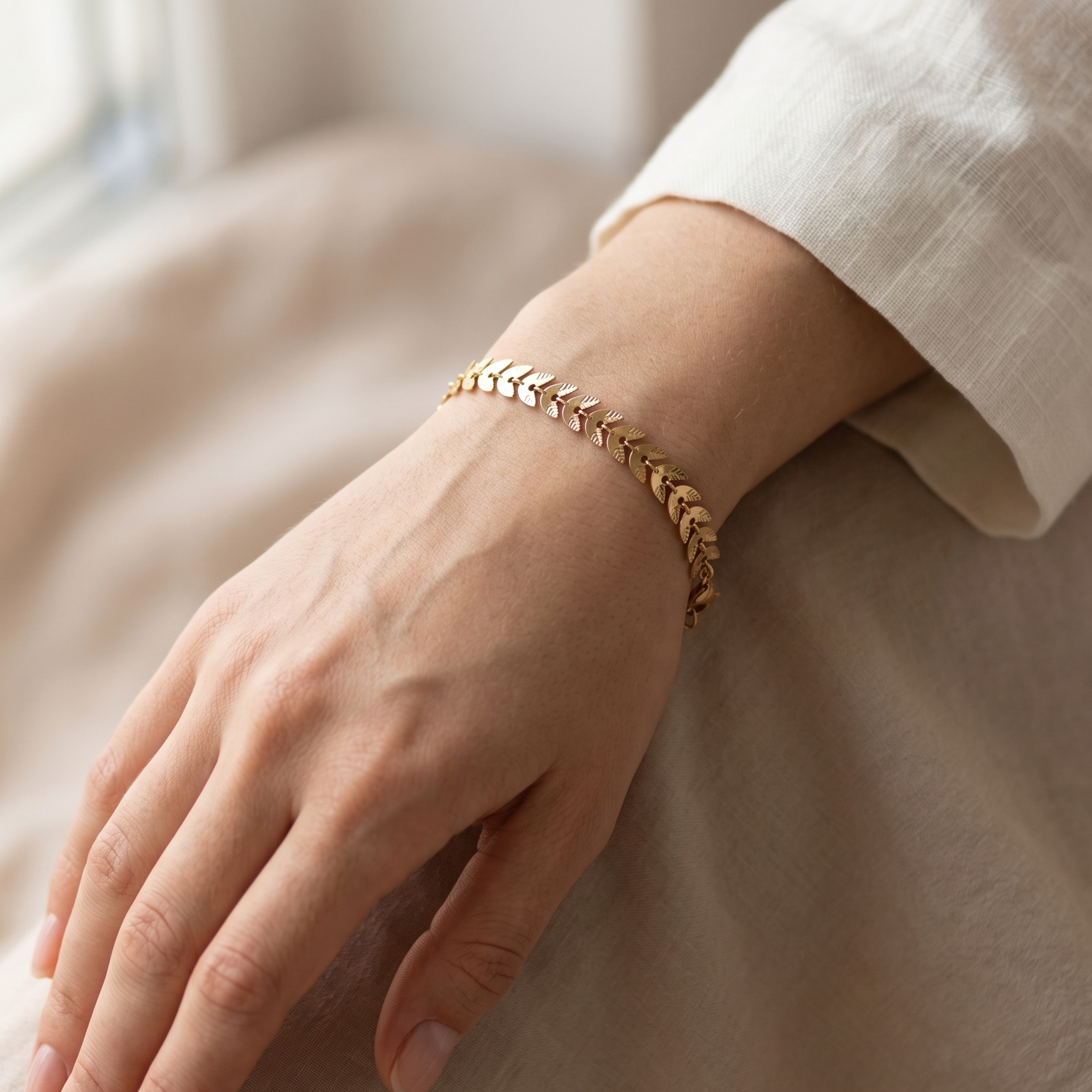 Hand wearing a gold bracelet on a neutral background