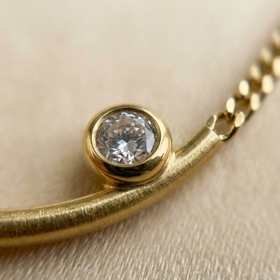 Gold necklace with a diamond on a beige background