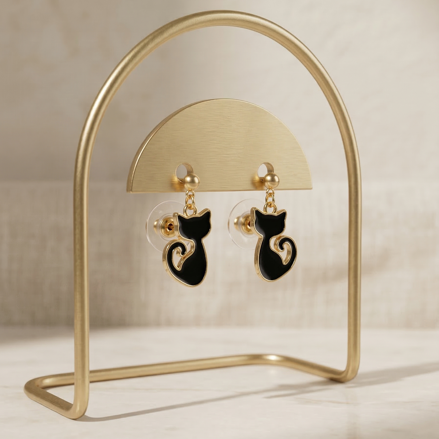 Cat-shaped earrings on a gold stand against a beige background