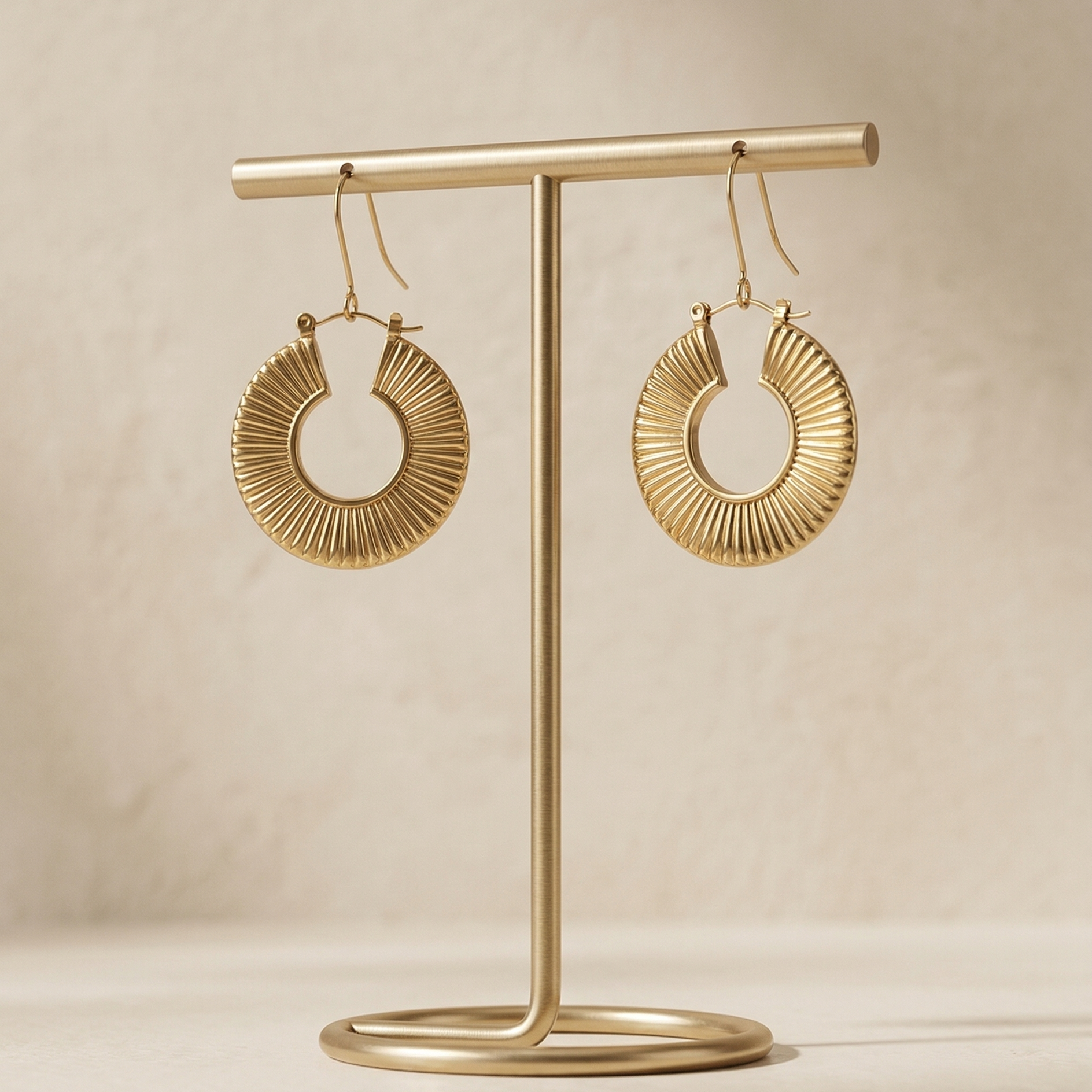 Gold hoop earrings on a matching gold stand against a beige background