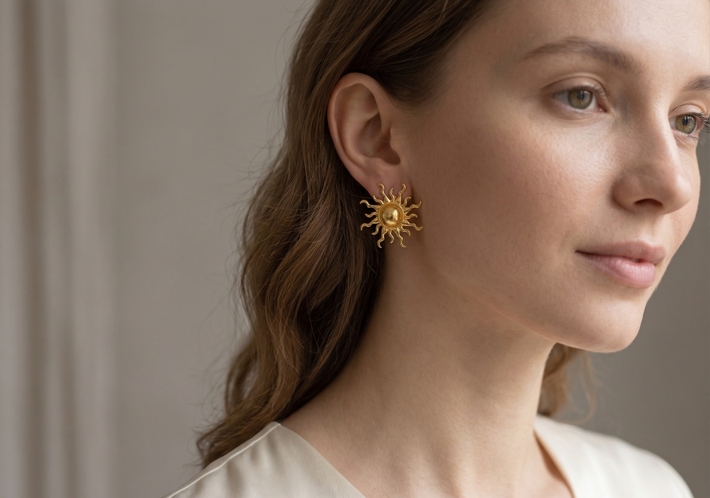 Woman wearing gold sun-shaped earrings against a neutral background