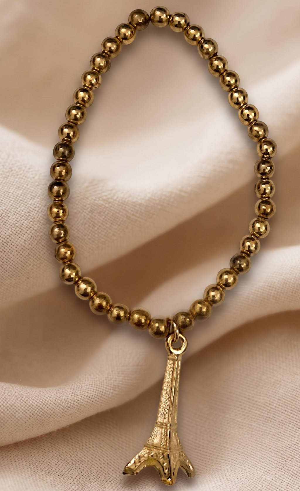 Gold beaded bracelet with a bird charm on a beige fabric background
