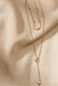 Gold necklace with heart pendant on a beige fabric background