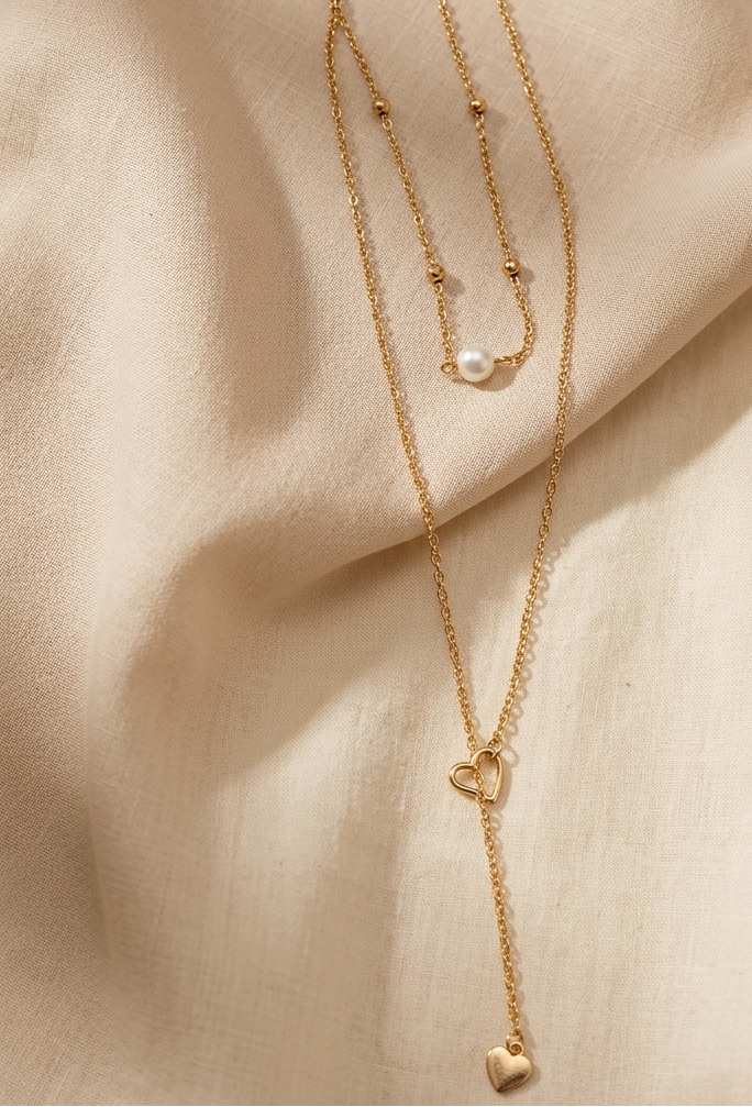 Gold necklace with heart pendant on a beige fabric background