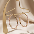 Gold hoop earrings with pink gemstones on a beige background