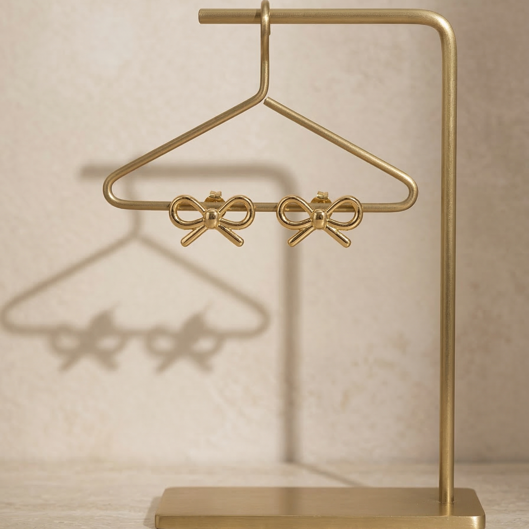 Gold jewelry stand with bow design on a beige background