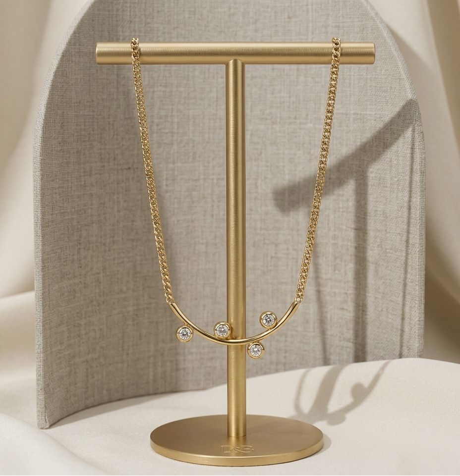Gold necklace on a gold T-shaped stand against a neutral background