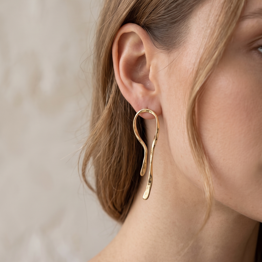 Close-up of a person wearing gold hoop earrings with a neutral background