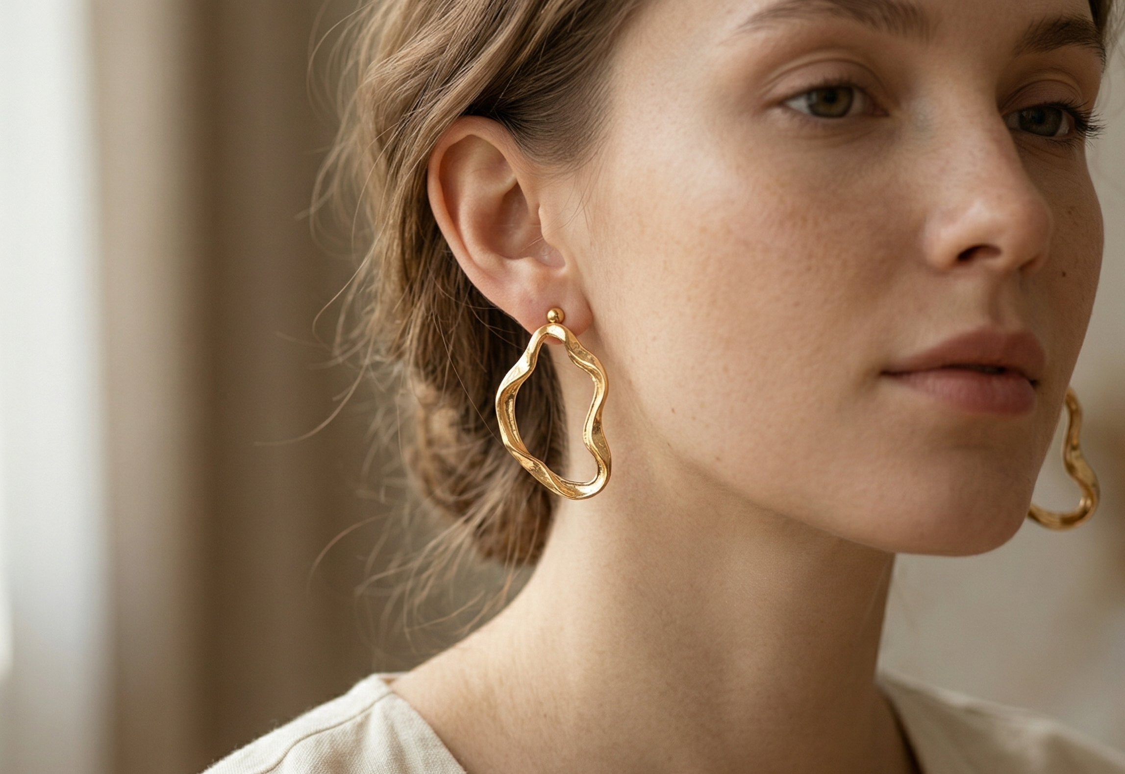Woman wearing gold hoop earrings with a neutral background