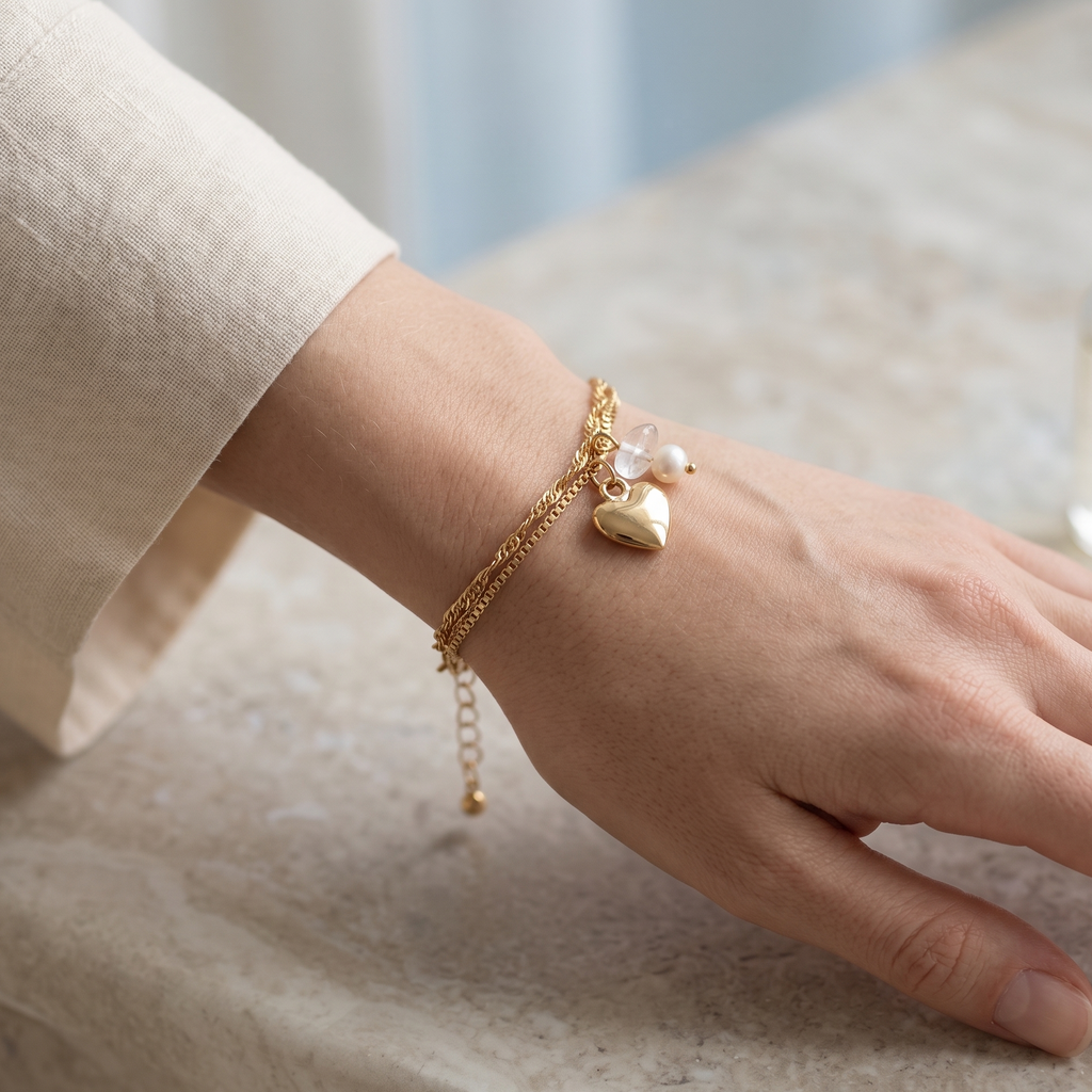 Hand wearing a gold bracelet with a heart charm on a neutral background
