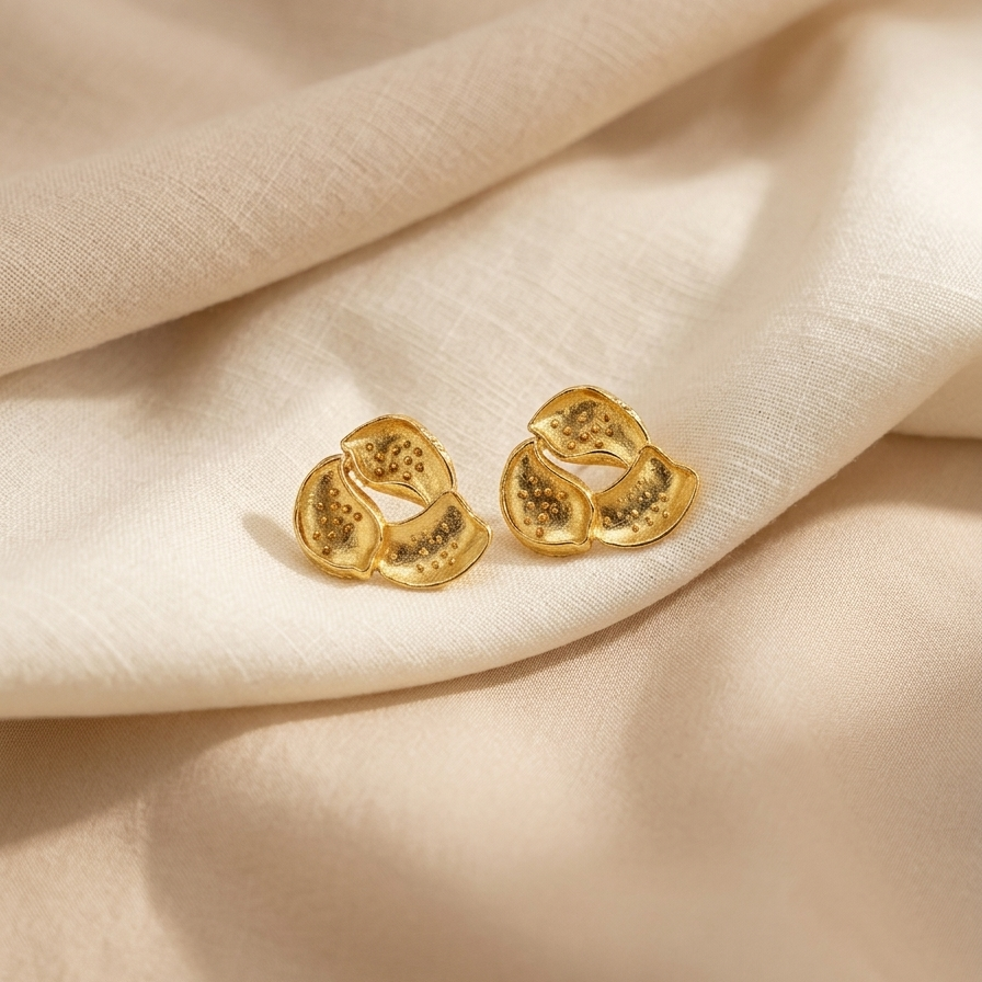 Gold earrings on a beige fabric background