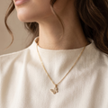 Close-up of a person wearing a gold necklace with a delicate pendant on a neutral background