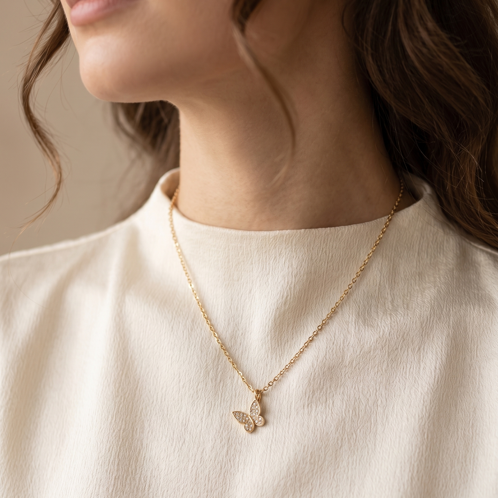 Close-up of a person wearing a gold necklace with a delicate pendant on a neutral background