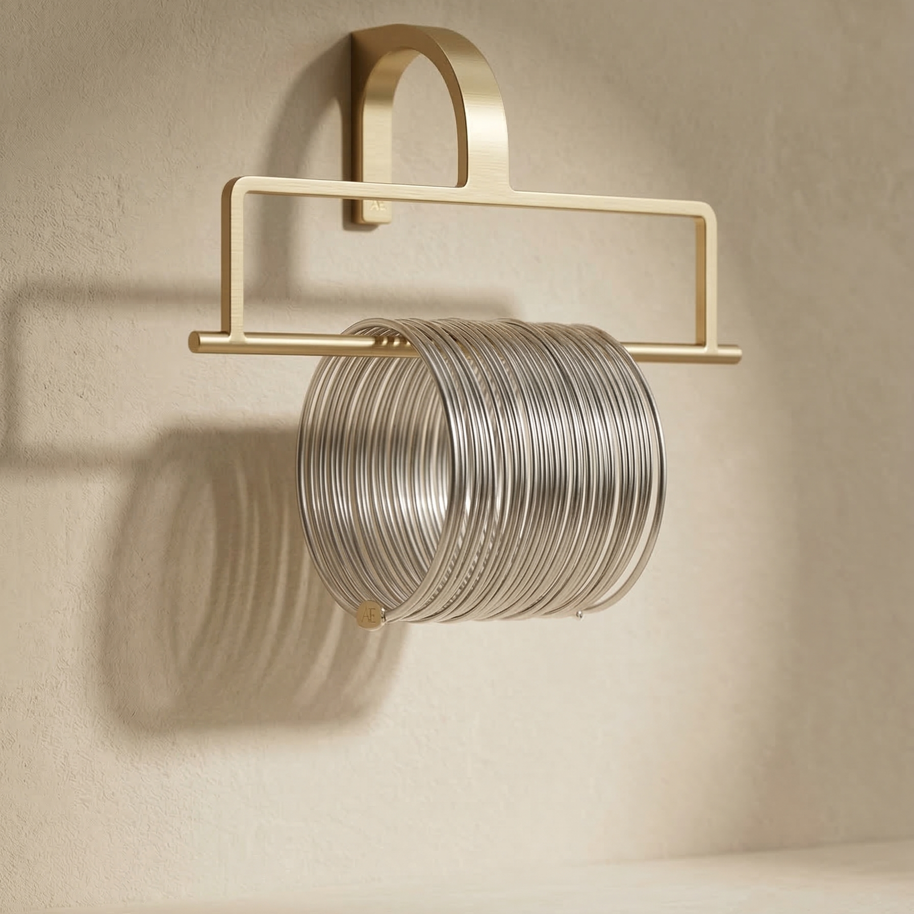 Gold wall-mounted jewelry holder with silver rings on a beige wall.