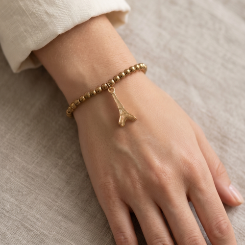 Hand wearing a gold bracelet on a neutral background