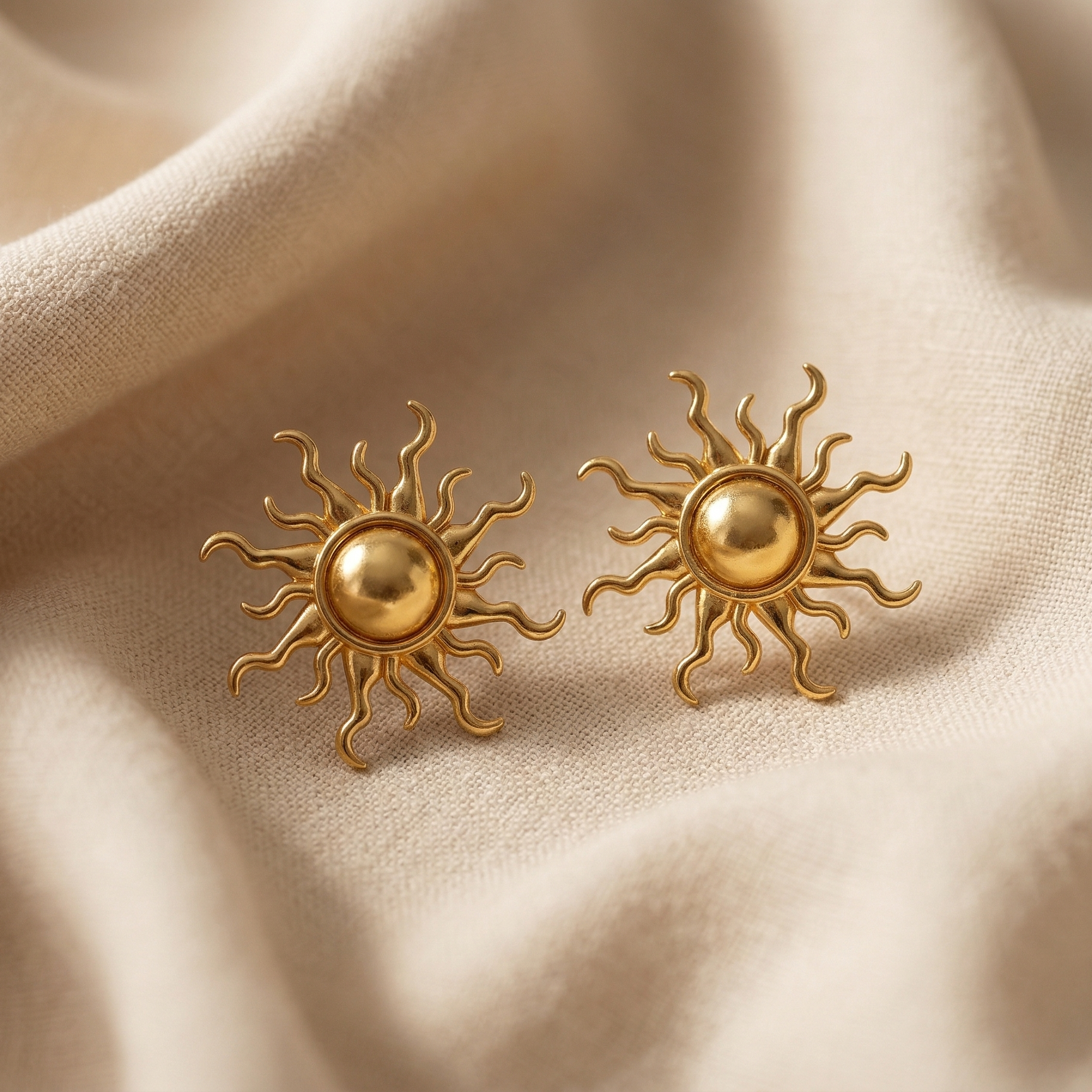 Gold sun-shaped earrings on beige fabric