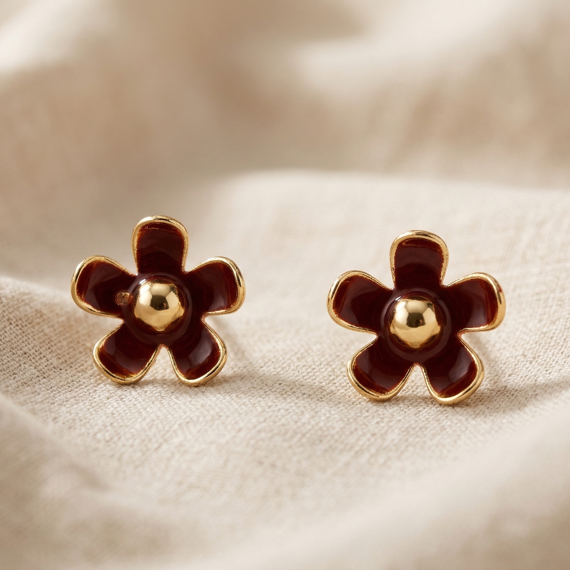 Pair of flower-shaped earrings with gold centers on a beige fabric background